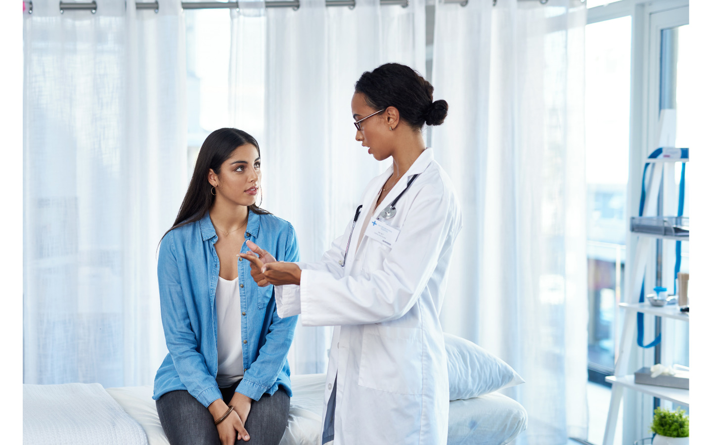 Vrouw met blauwe blouse op consultatie bij vrouwelijke gynaecoloog met witte jas.